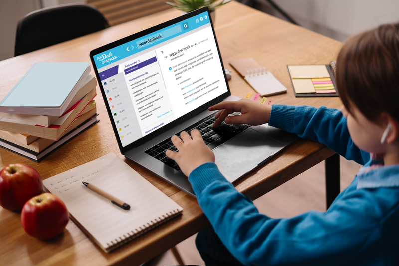 Een kind zit aan tafel achter een laptop. Op het laptopscherm is Van Dale Online op school te zien met een definitie van het woord 'woordenboek'