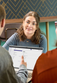 Een student zit tegenover twee andere studenten. In hun midden staat een laptop met op het scherm Van Dale Online.