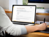 Een laptop staat op tafel met daarop een schermafbeelding van een deel van de uitleg uit de Van Dale E-learning Werkwoordspelling