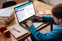 Een kind zit aan tafel achter een laptop. Op het laptopscherm is Van Dale Online op school te zien met een definitie van het woord 'woordenboek' 
