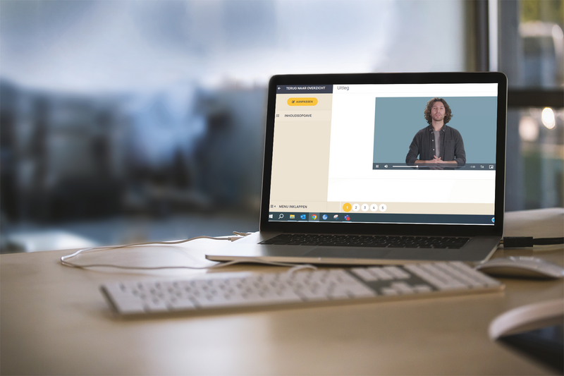 Een laptop staat op een tafel met een schermafbeelding van een uitlegvideo van de Van Dale E-learning werkwoordspelling